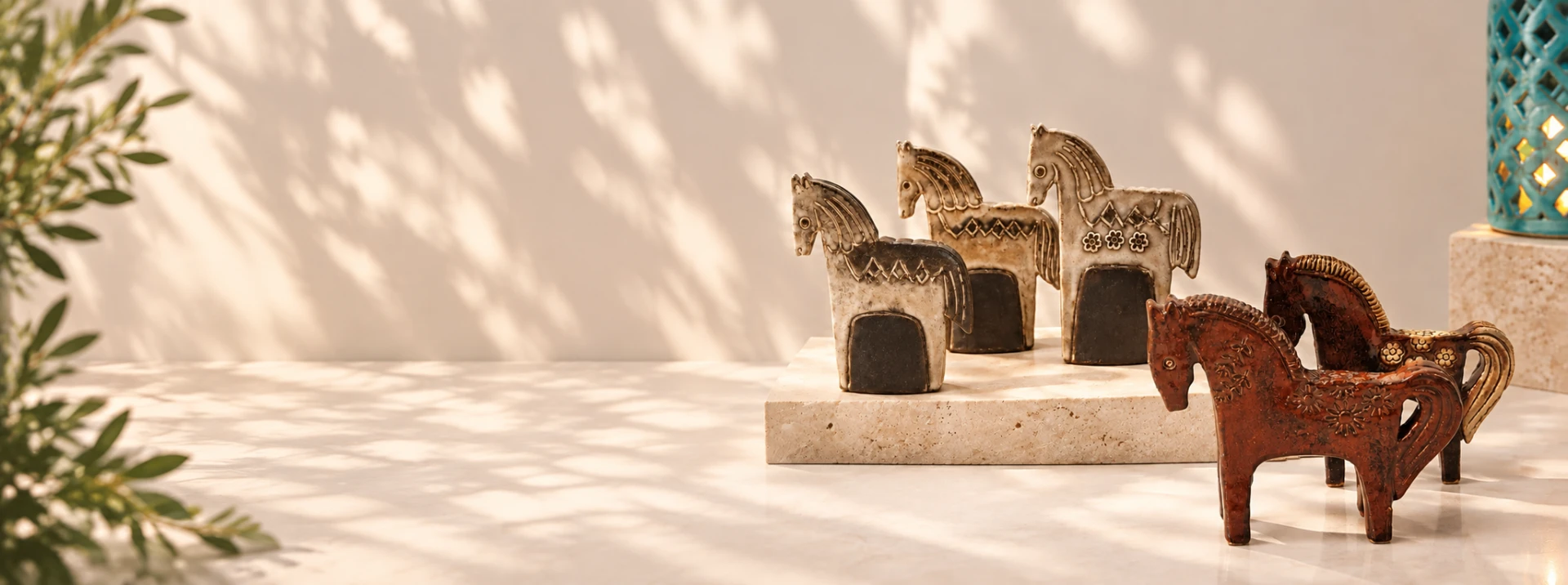 Five ceramic horse sculptures arranged on pale stone plinths in a sunlit studio setting